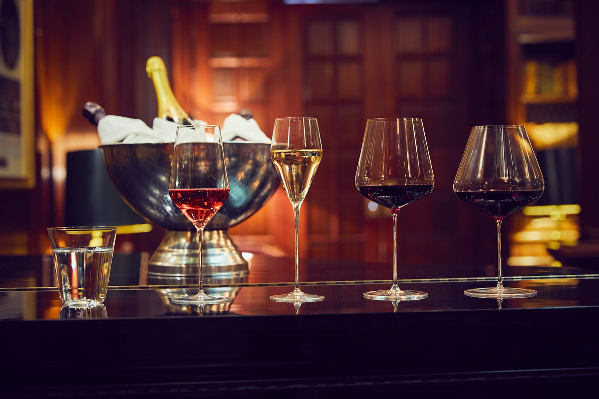 Zalto glasses of water, rosé, Champagne and red wine on a bar counter beside a Champagne bucket