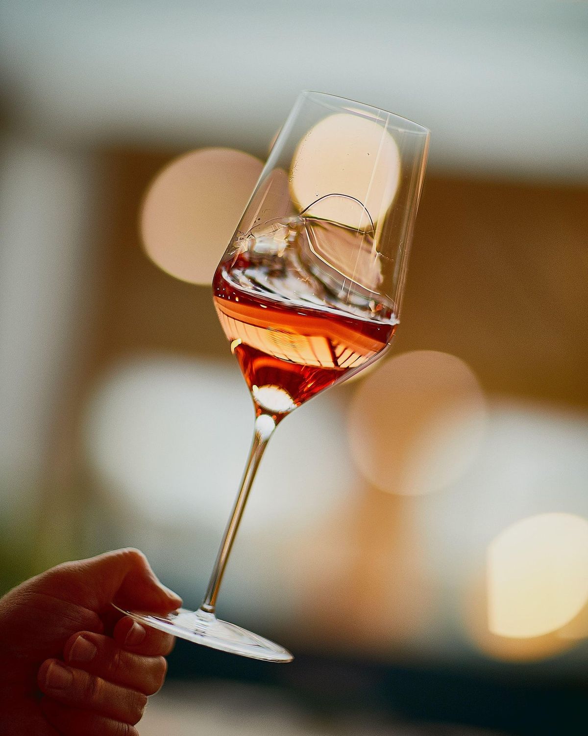 Hand holding a Zalto White Wine glass of rosé wine against soft lights