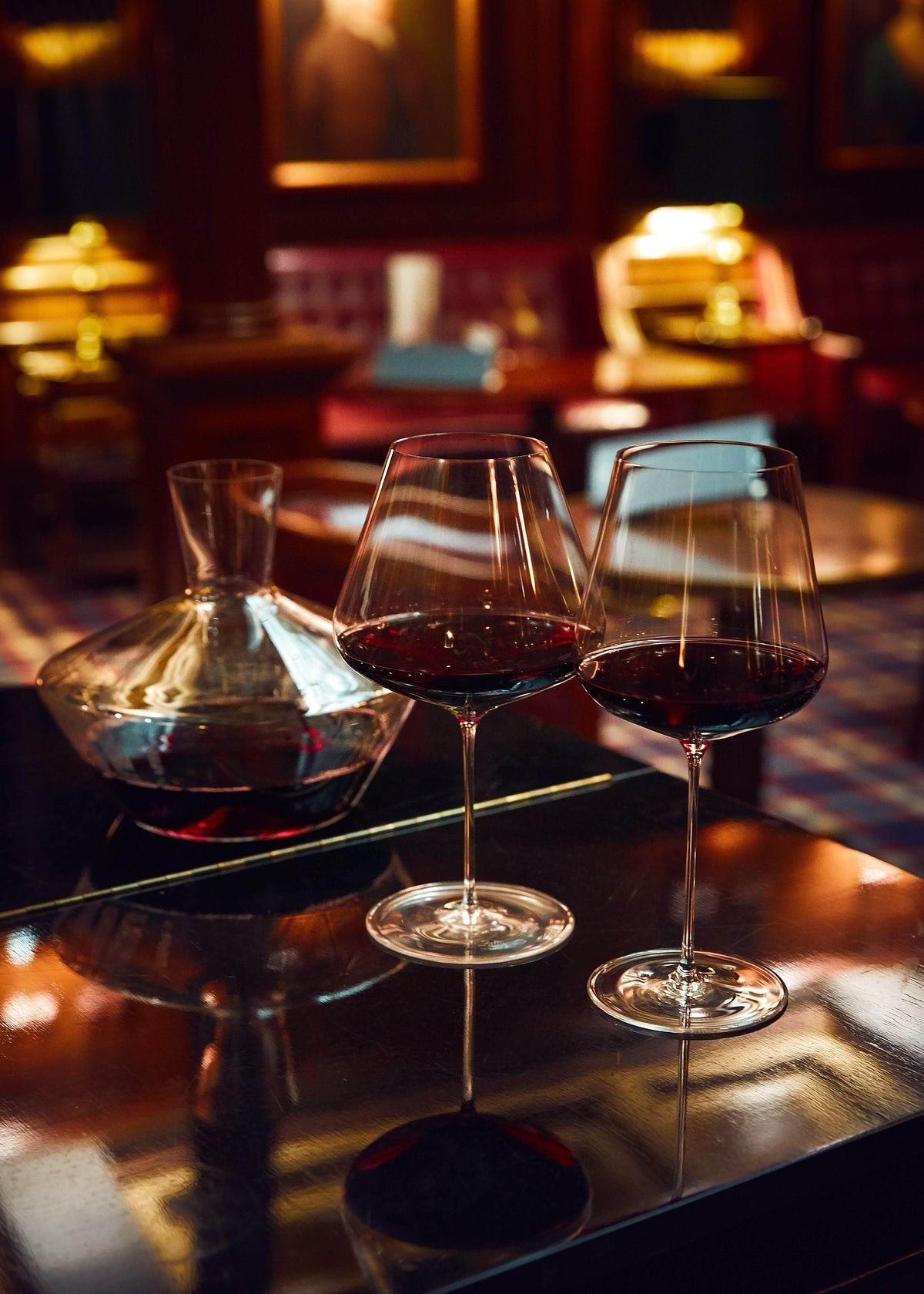 Zalto Burgundy glasses and a decanter of red wine on a bar counter